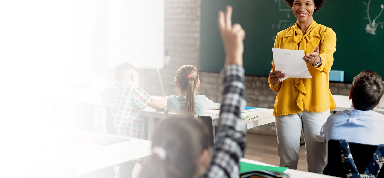 Experienced educator raising her hand in a classroom with engaged students